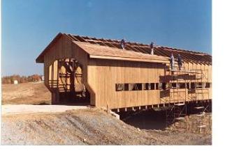 The longitudinal view shows four workers (two on scaffolding and two on the trusses) installing wood shingles on the roof.