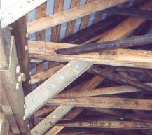 Because the trusses had shallow depth and caused higher chord forces, the picture shows more substantial roof bracing. Traditional knee braces between the sides of the lattice elements to the underside of the tie beams were augmented with longer elements beside and above the knees with the older, shorter elements bolted to the side of the extensions and then joined at the peak.