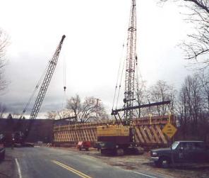 The picture shows two cranes holding the lattice truss vertically being positioned from the adjacent bypass bridge.