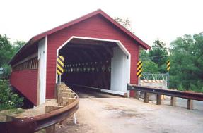 The picture shows the completed bridge with a lattice truss, the diagonal cut portal opening, the protective curbing and the metal approach rails.