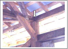 In this interior view the arrow points to the three-way connection of the rafter plate above the top chord with the tie beams connected to the tops of the vertical posts.