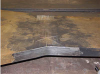 The photo shows a side view of field specimen FG38K-TF2-TopF-FCM with the weld oriented vertically. The specimen is comprised of a wider plate on the left and a more narrow plate on the right.