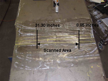 The photo shows a plan view of field specimen G2G-CF1-FCM with the weld oriented horizontally. The specimen is comprised of a wider and thicker plate to the top and a thinner and narrower plate to the bottom of the photo. The area of the weld between 224.79 and 795.02 millimeters (8.85 and 31.3 inches) is labeled because this area was scanned by the P-scan system. Note that 1 inch equals 25.4 millimeters.