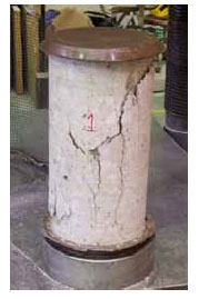 Figure 14. Photo. Concrete cylinder tested as part of the bogie vehicle impact test series. This is a post-test photo of a concrete cylinder, with capped ends, which was tested in compression. A slight diagonal band of fracture is evident, which is more dominant on the top half than on the bottom half.