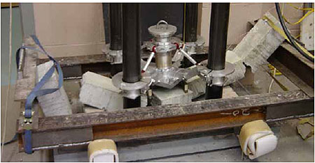 Figure 52. Photo. All plain concrete specimens impact the bottom of the test fixture. This is a post-test photo of a plain concrete beam. The beam is broken into about five pieces. It is resting on the bottom of the test fixture, with the impactor sitting on top of it. The end straps are visible on each end of the beam.
