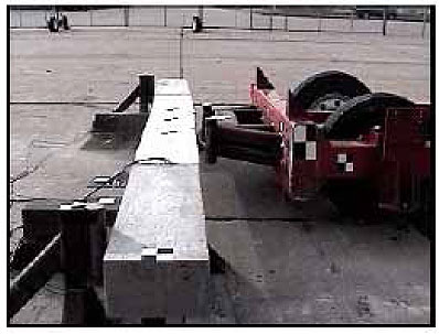 Figure 77. Photo. The beam rebounds when impacted at 8.6 kilometers per hour (5.3 miles per hour), pushing the bogie vehicle backward. One shapshot from a side view video shows the beam in reverse flexure. The beam is intact and not broken. A small gap is visible between the beam and load frame, indicating that the beam has slid on its supports. A small gap is also visible between the beam and the bogie vehicle impactors, indicating lost contact.