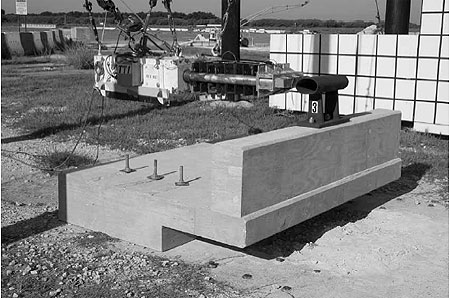 Figure 85. Photo. Parapet before test P3. This pre-test photo shows the setup of the pendulum as it hangs from cables. The 10 stages of honeycomb are visible. Also shown is the field side of the bridge rail, which is attached by bolts to the reinforced concrete parapet and deck. The back portion of the deck is cantilevered above the ground.