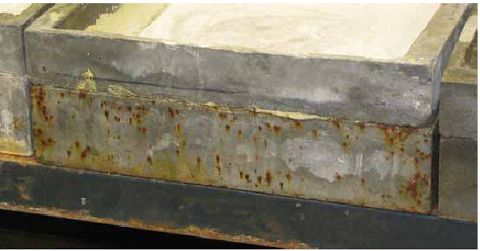 This photo shows the surface of the side of a U H P C scaling slab. This vertical surface has been exposed to an extremely intense environment of freezing and thawing with intermittent wetting by chloride contaminated water. Rust staining is visible on the surface. This staining results from the corrosion of steel fibers that were exposed to the surface due to air bubbles that were trapped along the edge of the mold during casting. There is no other visible damage.