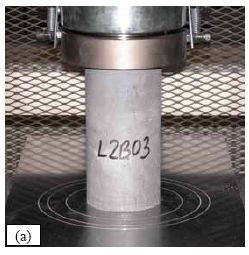 (a) shows a 76-millimeter diameter cylinder being tested in a compression testing machine. (b) shows a 100-millimeter cube being tested in a compression testing machine.