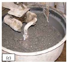 This series of five photos graphically depicts the stages in the mixing of U H P C as observed for all of the batches of concrete cast for this study. (a) shows the dry constituent materials in the pan mixer as the water is being added. (b) shows the U H P C in the mixer as the H R W A is added. (c) shows the U H P C before its conversion into a viscous paste. (d) shows the U H P C at the time of fiber addition. (e) shows the U H P C after mixing is complete.
