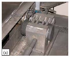 (a) shows a 76-millimeter diameter cylinder held in the grips of a grinding machine as the diamond grinding blade is making a perpendicular pass to smooth the surface. (b) shows the dial gage, stand, and milled plate that were used to verify the planeness and parallelness of the ends of the cylinders