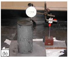 (a) shows a 76-millimeter diameter cylinder held in the grips of a grinding machine as the diamond grinding blade is making a perpendicular pass to smooth the surface. (b) shows the dial gage, stand, and milled plate that were used to verify the planeness and parallelness of the ends of the cylinders