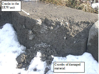 Figure 49. Photo. Freeze-thaw damage on SRW unit in field. The picture has a caption of the cracks in the SRW unit, with an arrow pointing to the top of a unit with a long crack. There is a caption pointing to crumbs of damaged material at the bottom of the unit.