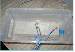 Figure 90. Photo. Water surrounding specimen and specimen (as graphed in figure 89). The photo is container holding a specimen with attached wires to the container and specimen.