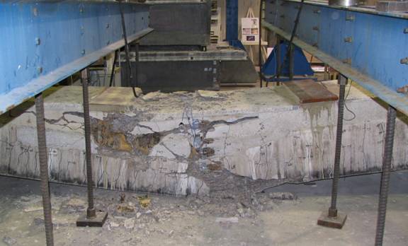 Figure 16. Photo. Failed Beam 4. This photo shows this beam after failure. The beam is observed to have failed at midspan with significant spalling on the vertical elevation and on the top flange. The impact of the beam on the floor caused additional damage to the bottom flange.