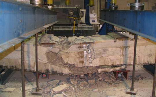 Figure 24. Photo. Failed Beam 14. This photo shows this beam after failure. The beam is observed to have failed at midspan with significant spalling on the vertical elevation and on the top flange. The impact of the beam on the floor caused additional damage to the bottom flange.