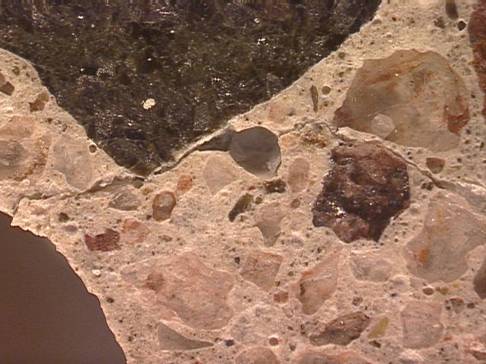 Figure 7. Photo. Photomicrograph of a crack near the exposed surface of the concrete. This photo shows a discrete crack extending away from the exposed bottom face of the beam running toward the interior of the beam. At this location the crack tends to pass through the paste.  The crack is approximately 0.025-millimeter (0.001-inch) wide.Figure 7. Photo. Photomicrograph of a crack near the exposed surface of the concrete. This photo shows a discrete crack extending away from the exposed bottom face of the beam running toward the interior of the beam. At this location the crack tends to pass through the paste.  The crack is approximately 0.025-millimeter (0.001-inch) wide.