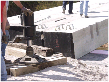 Photo showing black bitumen coating on the end of several concrete beams being placed on the geosynthetic reinforced soil (GRS) abutment.