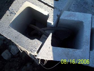 The photo is a downward view at the corner where the abutment face and wing wall meet to form an obtuse angle (greater than 90 degrees). The photo shows that the corner blocks are cut to form the angle, and the inside web of hollow-core block is notched so that a bent piece of rebar can be inserted into the core of the adjacent block's segment.