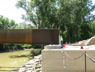 The photo shows the placement of steel girders on a cast-in-place (CIP) footing bearing on the beam seat of a large geosynthetic reinforced soil (GRS) abutment.