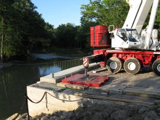 The photo shows a large crane set up at the face of a geosynthetic reinforced soil (GRS) abutment. The outrigger is supported on a bearing pad placed at the face of the wall.