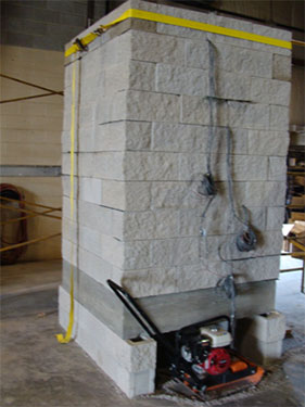 Figure 16. Photo. DC-1 GRS PT (before testing). Angled side view of Definance County pier setup before testing. The base pad is elevated on concrete masonry unit blocks to make room for a bottom set of bolted channel beams. A vibratory plate compactor appears immediately adjacent to the pier in this photograph.