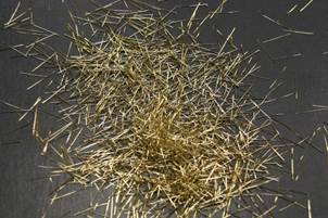 This photo shows a few hundred brass-colored steel fibers dropped onto a tabletop. It illustrates the geometry of the steel fiber reinforcement commonly used in ultra-high performance concrete.