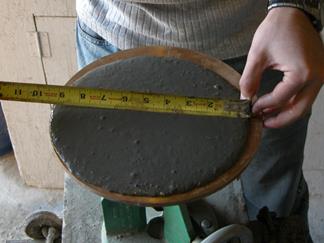 This photo shows the execution of the ASTM C1437 flow test. The diameter of the ultra-high performance concrete circle is being measured.