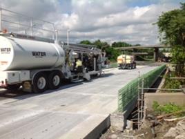 This photo shows the equipment used to profile the surface of a bridge deck after re-decking with precast concrete deck panels and field-cast ultra-high performance concrete connections. The truck-size equipment is profiling a lane width at a time.