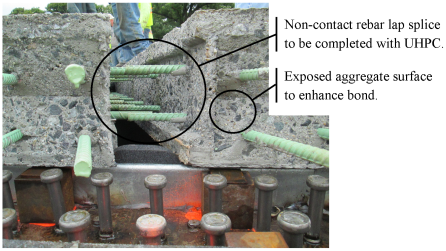 This photo shows the deck-level connection between two adjacent precast concrete deck panels immediately above a girder line. The photo is a transverse view across the bridge at the level of the deck. The lap-spliced reinforcing bars and the exposed aggregate concrete surface finish are visible along with the haunch formwork and the tops of the steel shear studs.