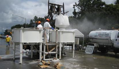 This photo shows a pair of portable mixers operating on a bridge deck reconstruction site. One mixer is being loaded with constituent materials, and the other mixer is mixing a separate batch of ultra-high performance concrete.