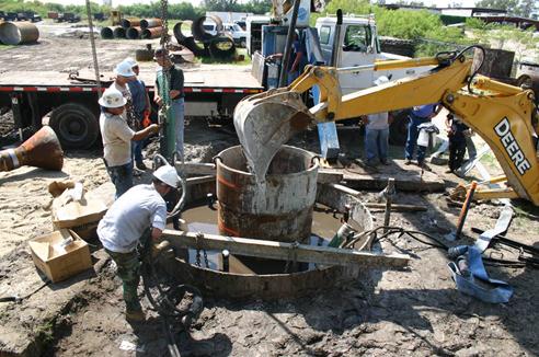 This photo shows a back-hoe holding the central casing in place. In lieu of welded centralizing struts from the central casing to the surface casing, the contractor opted to secure the top of the central casing with a back-hoe bucket continually manned by an operator. The base of the casing had already been secured by the self-weight cutting into the soil.