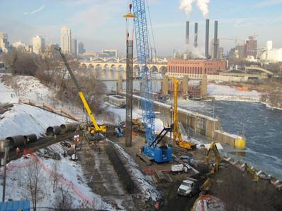 This photo shows an overview of the work site. The reinforcement cages for the I-35W bridge pier 2 bridge shafts (south side of river) were fabricated onsite (left-center) and hoisted by a crane for insertion into the excavation adjacent the river bank (right).
