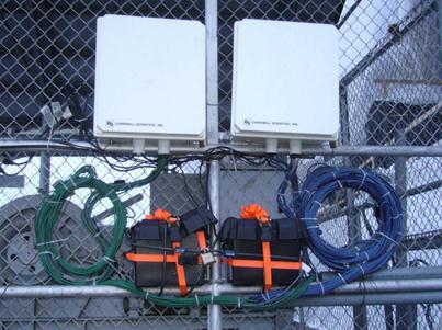 The photo shows two of the three environmental enclosures used to house the monitoring systems. The construction load monitoring systems with both types of gauges: (1) vibrating wire (VW), which were blue and (2) resistance (RT), which were green, were installed temporarily on a nearby fence.