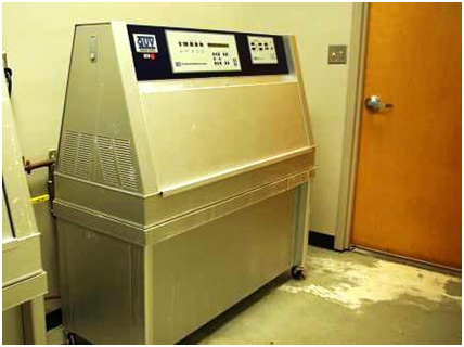 This photo shows an ultraviolet (UV) weathering tester, which is a large apparatus on four wheels. Test panels are loaded into the UV weathering tester from the sides. Test panel specimens are installed in the test machine so that they form the side walls of the test chamber. The chamber also consists of a water reservoir, which is heated to produce the water vapor for condensation. The source of UV is light from 340-nm lamps.