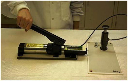 This photo shows a hydraulic adhesion tester. The tester consists of a cylindrical enclosure that transfers the pumping action of the handle. The hydraulic force is transferred to a coupling fixture, which attaches to the dolly to pull it away from the surface of the coating system.