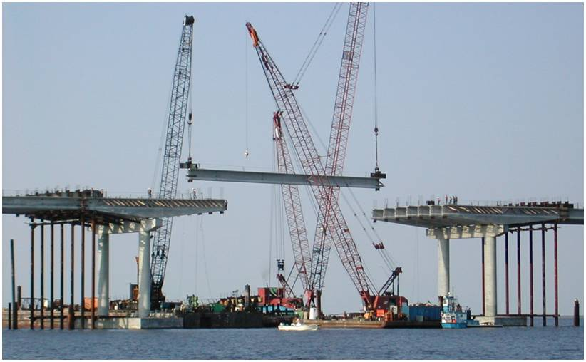 Figure 19. Photo. Precast spliced girder bridge during erection. This photo shows a precast spliced girder bridge during erection over a body of water. Cranes are being used to attach parts of the bridge