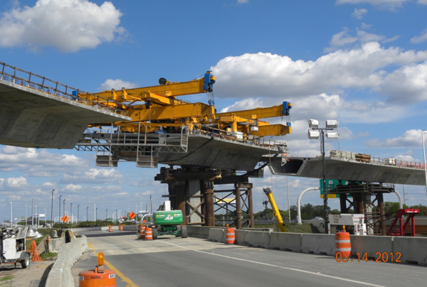 Figure 22. Photo. Precast segmental balanced cantilever bridge erection using a segment lifter. This photo shows a precast segmental balanced cantilever bridge being erected over a highway using a segment lifter