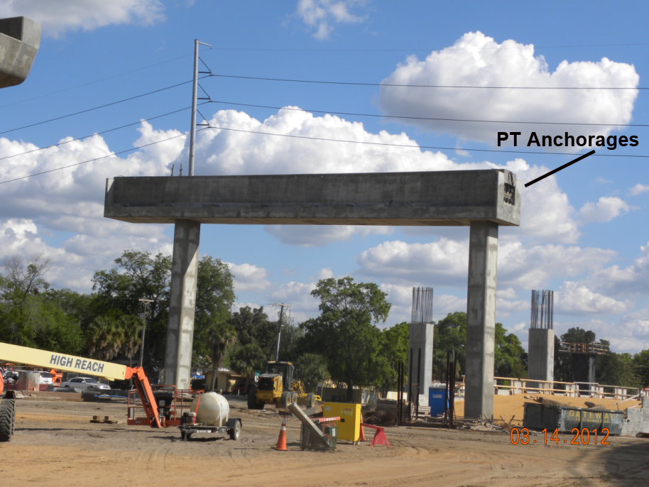 Figure 27. Photo. PT straddle bent during construction. This photo shows a post-tensioned (PT) straddle being bent during construction. PT end anchorages are identified at both ends of the PT straddle