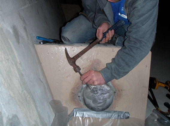Figure 54. Photo. Grout sample acquisition at an opened internal tendon end cap by light chipping. This photo shows a worker removing a permanent grout cap from the end of an internal tendon at a blister using a large screwdriver and hammer.