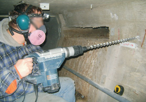 Figure 56. Photo. Internal tendon access at an intermediate location by drilling. This photo shows a worker with a power drill excavating concrete on a vertical surface in order to access an internal tendon.