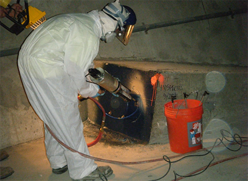 Figure 77. Photo. Applying elastomeric coating over a grout cap. This photo shows a worker applying an elastomeric coating to a previously opened grout cap on an internal tendon.