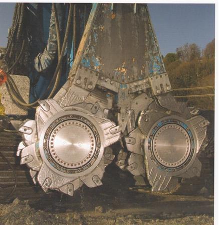 This photo shows cutter soil mixing (CSM) cutter wheels. There are vertically oriented cutting blades on the bottom of shaft and cutting teeth.