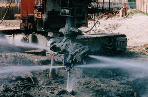 This photo shows an example of a wet jet end (WJE) tool. The end of a shaft mixing tool with treated soil on paddles is shown with water jets emanating from the outer edge of paddles and the bottom of the shaft.