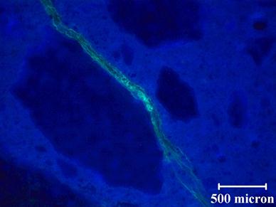 The photo shows a polished section for the same concrete prism (different section) as in figure 56. When comparing the images in the photos, there does not appear to be any evidence of loss of alkali-silica reaction gel. This figure shows a relatively large crack that still stained after polishing. When comparing the quality of the images, the unpolished section (see figure 56) does not appear as clear as the polished section in this figure. The image here is not only in focus but the stained features are more distinct. It is possible to see microcracks at the edge of the macrocrack. Based on these results, for future petrographic examination, the samples will be polished before staining.