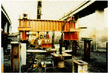 The figure shows a full-scale load test set-up in California, which was designed to study the engineering behavior of individual micropiles and micropile groups and/or systems under axial and transverse load response modes. The set-up includes a large reaction frame.