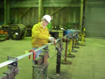 This photo shows a wire strand under construction. The worker in the picture is making sure that the wires are parallel and is tightening a steel clamp. 