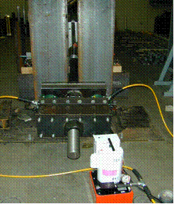 This photo shows a hydraulic pump in the foreground with the hydraulic jacks shown placed between the cable mockup structure and the jacking beam. 
