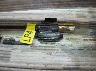 This photo shows linear polarization resistance (LPR) sensor 4 as found during cable disassembly. The sensor is seen sitting on the second strand. The sensor head is not covered; however, the stainless steel pipe is intact and located directly behind the sensor head itself. The strands surrounding the sensor have white salt and zinc corrosion product present. 