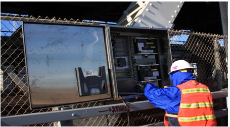 A worker is seen wiring the Sensor Highway II data acquisition system (DAQ). The system is located at the sidewalk level below the bridgeâ€™s on-ramp.